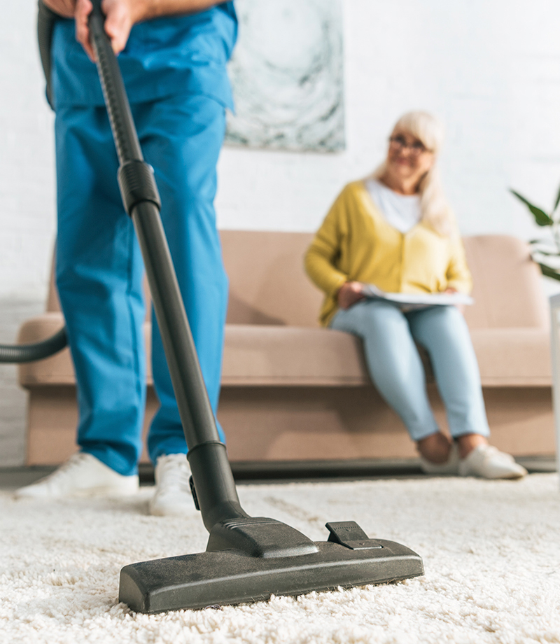 rajattu kuva miehestä, joka käyttää pölynimuria vanhemman naisen istuessa sohvalla