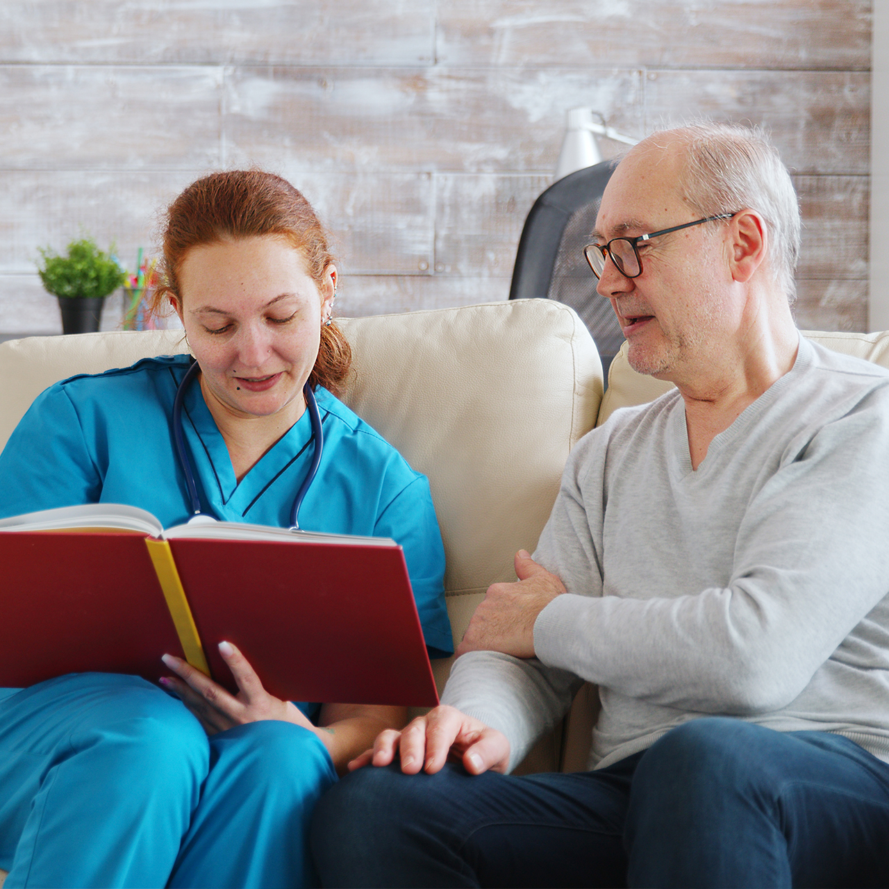 Sosiaalityöntekijä lukee vanhalle ja vammaiselle miehelle, joka istuu sohvalla